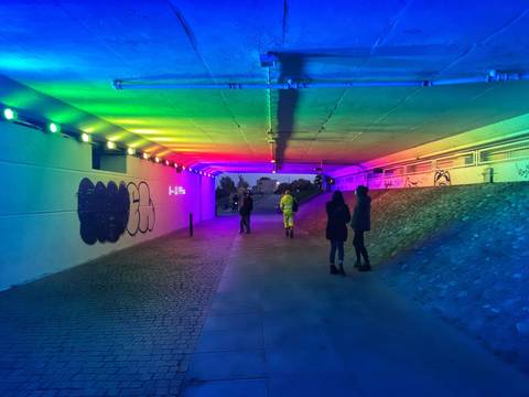 Underground passage lit with rainbow LED lights and pedestrians strolling through.