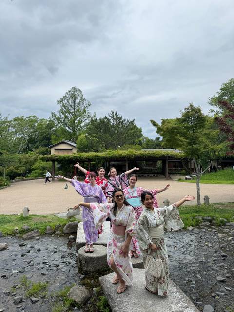 Group of women in colorful yukata pose happily in a Japanese garden courtyard with lush greenery.