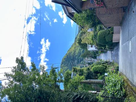 Steep residential lane climbing a green mountain with power lines against a bright blue sky.