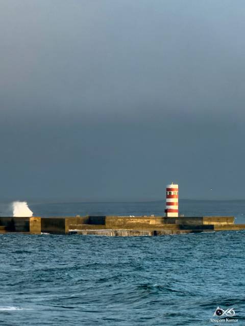 Minimalist view of a striped lighthouse on a breakwater with ocean horizon.