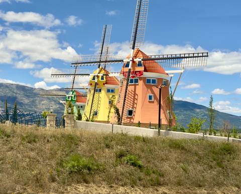 Brightly painted decorative windmill structures set against mountains and blue sky.