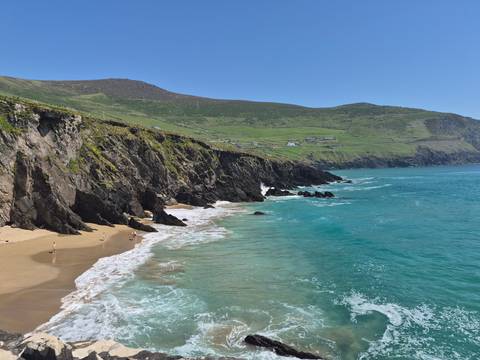 Turquoise waves hitting rugged cliffs and sandy beach along Slea Head Drive.