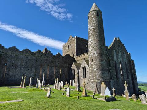 Medieval stone ruins of a cathedral and round tower surrounded by ancient gravestones.