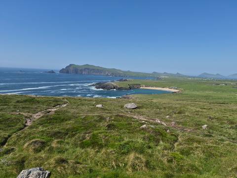 Wide coastal panorama of green headlands, sandy cove and rolling Atlantic surf.