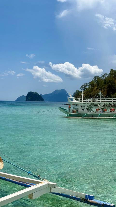 White outrigger boat floating on turquoise sea with limestone islands in the distance.