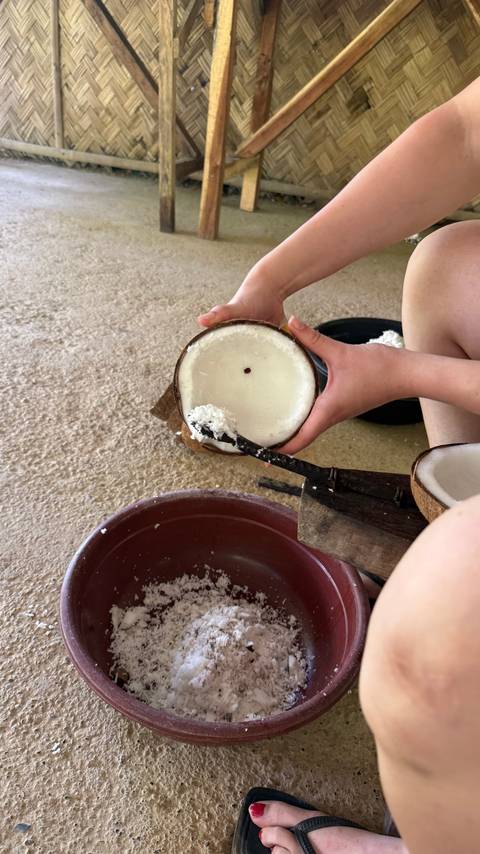 Hands scraping fresh coconut meat into a bowl during a traditional food preparation activity.