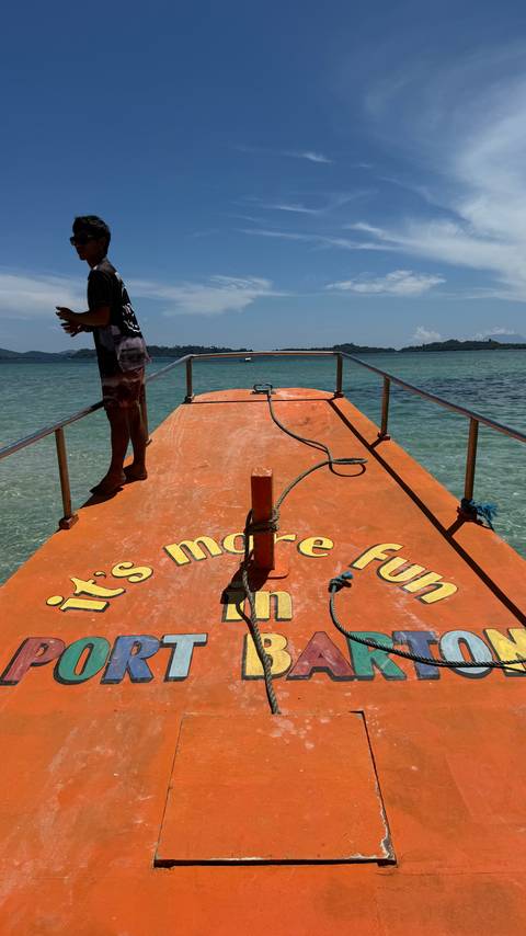 Bow deck of orange tour boat with slogan, clear aqua water and distant islands under bright sun.