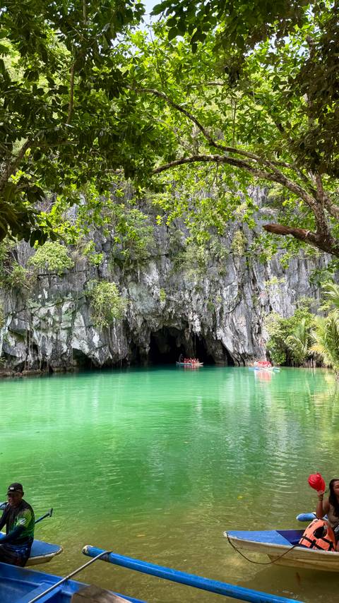 Emerald green lagoon leading into the dark cave entrance of the Puerto Princesa subterranean river with two paddle boats of visitors.