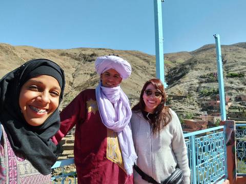 Three smiling travellers posing for a selfie with arid mountains and blue sky behind