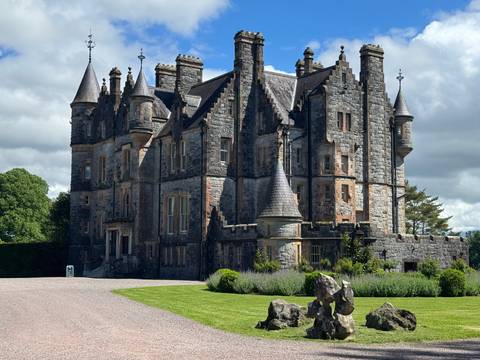 Stone castle with turrets and manicured lawn under partly cloudy sky
