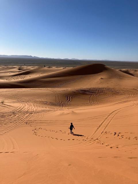 Vast rippled sand dunes with vehicle tracks and lone person walking across