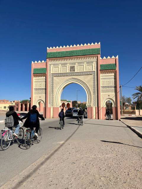 Cyclists ride through ornate Moroccan gate with tiled arch and pink walls