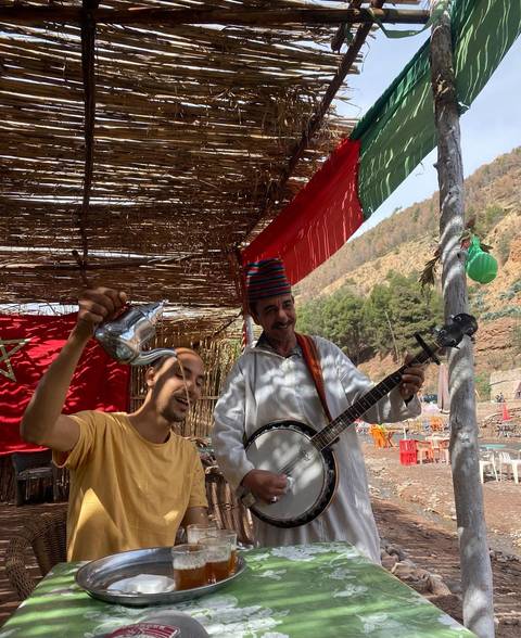 Local musicians under a reed canopy pouring tea and playing banjo in the Atlas Mountains