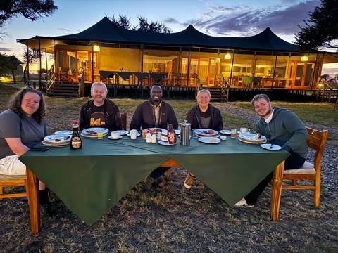 Travel group enjoying outdoor breakfast at safari camp at dawn