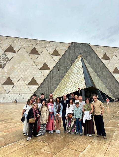Tour group standing in front of the modern pyramid-shaped entrance of the Grand Egyptian Museum.