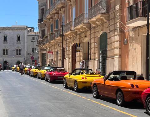 Row of colorful convertible sports cars parked along a historic Sicilian street.