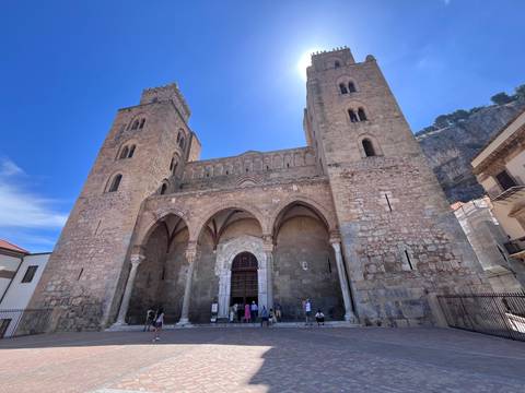 Front façade of Cefalù Cathedral with visitors gathered on the steps beneath twin towers.