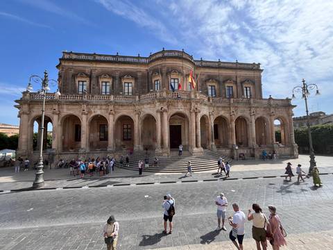 Grand baroque Palazzo Ducezio in Noto with visitors on the steps and plaza.