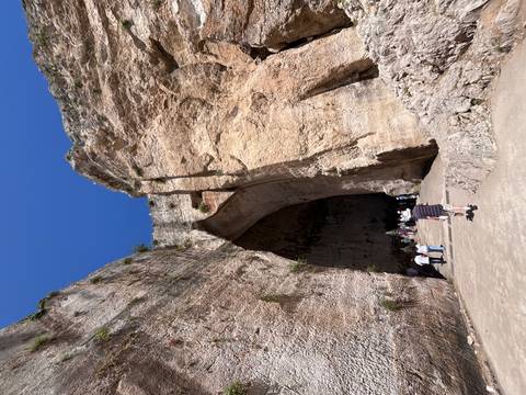 Visitors walking toward the towering entrance of the Ear of Dionysius cave in Syracuse.