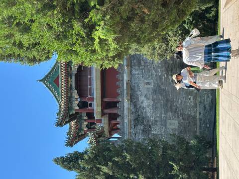 Tourists walking beside a red-walled palace tower in Beijing on a sunny day.