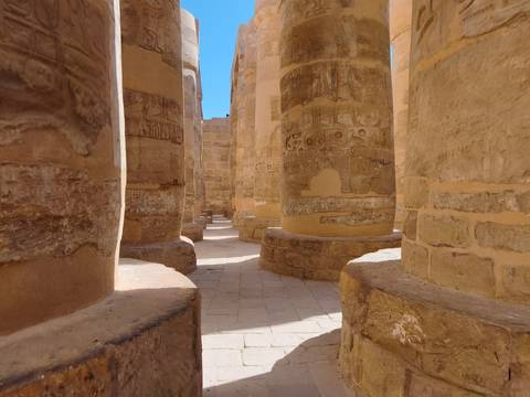 Massive sandstone columns carved with hieroglyphs inside Karnak Temple under bright sunlight.