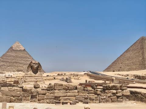 Iconic view of the Great Sphinx with two pyramids rising behind on a clear desert day.