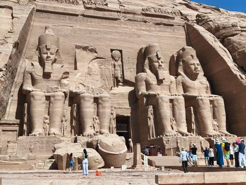 Grand statues of Ramses II carved into the rock façade at Abu Simbel with tourists below.
