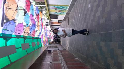 Woman poses in a narrow alley topped with rows of colorful hanging umbrellas.