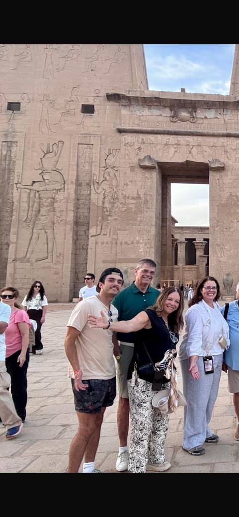 Tour group smiles outside massive carved columns of an ancient Egyptian temple complex.