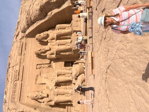 Visitors stand before the colossal seated statues of Abu Simbel carved into a sandstone cliff.