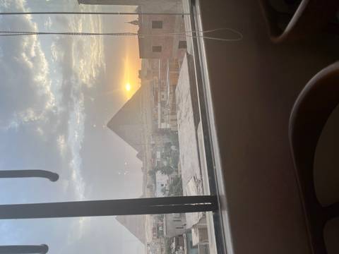 Sun sets behind the Giza Pyramid viewed through a bus window over city rooftops.