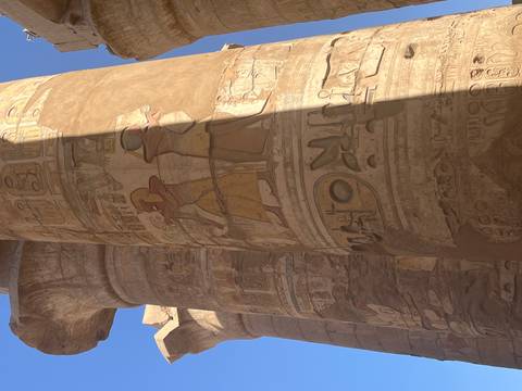 Sunlit section of a massive temple column covered in detailed hieroglyphs and figures at Karnak.
