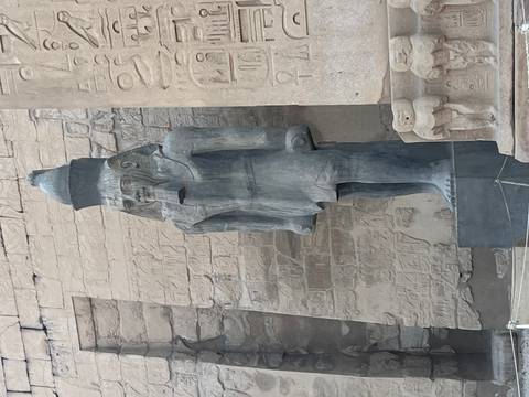 Close-up of a tall ancient statue of a pharaoh standing outside temple walls etched with reliefs.