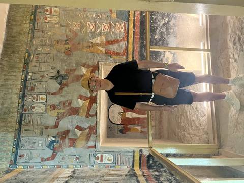 Man poses inside a richly decorated Egyptian tomb chamber with vivid wall paintings.