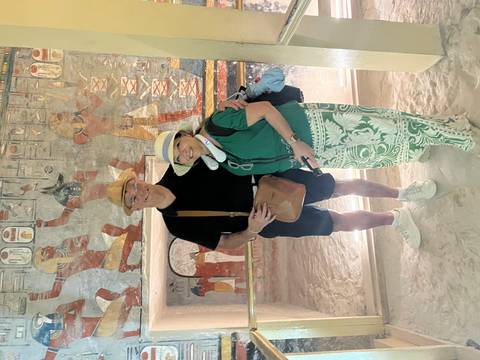 Couple stands together inside a tomb corridor decorated with colorful ancient Egyptian murals.