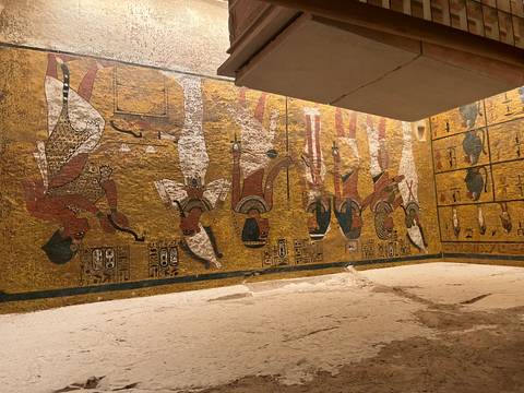 Wall of an Egyptian tomb featuring detailed scenes of deities and pharaohs painted on a golden background.