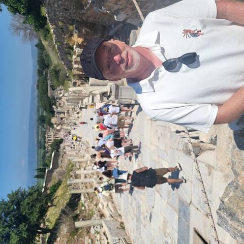 Tourists walk the ancient marble street of Ephesus with ruins stretching into the distance.