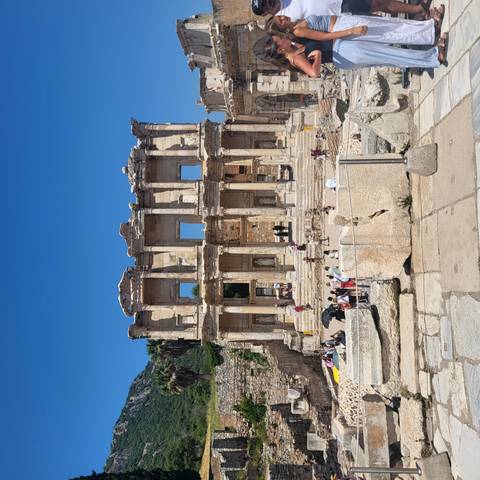 Front view of the Library of Celsus with visitors scattered on the steps under clear skies.