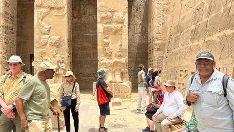Visitors explore hieroglyph-covered columns inside an ancient Egyptian temple.