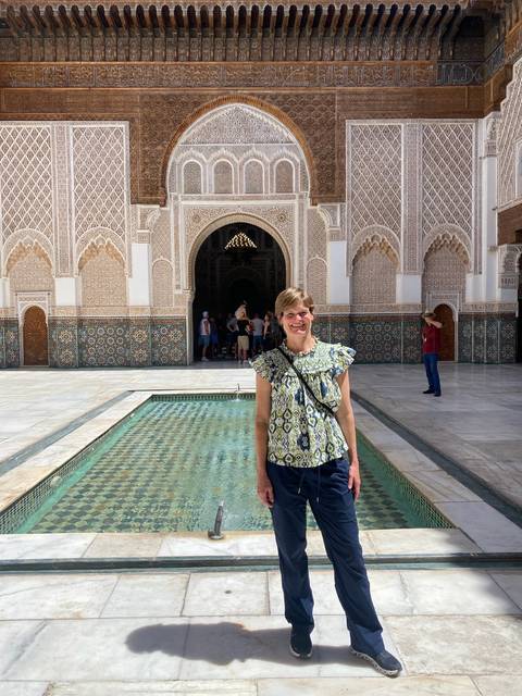 Traveler stands beside a tiled fountain in a historic Moroccan madrasa courtyard.