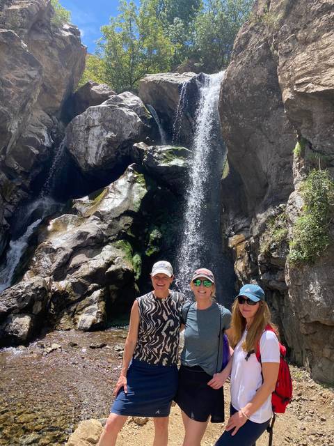 Three travelers smile in front of a tall mountain waterfall.