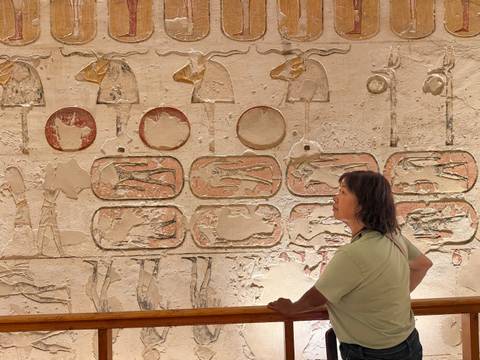 Visitor observes detailed sunken reliefs and cartouches on an ancient Egyptian wall.