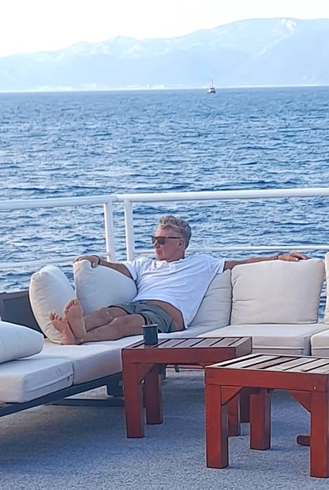 Man lounges on cushioned deck seating of a yacht with the Adriatic Sea beyond.