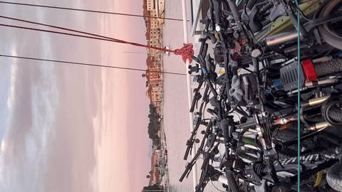 Dozens of bicycles stacked on the deck of a boat at pink sunset over a harbor.