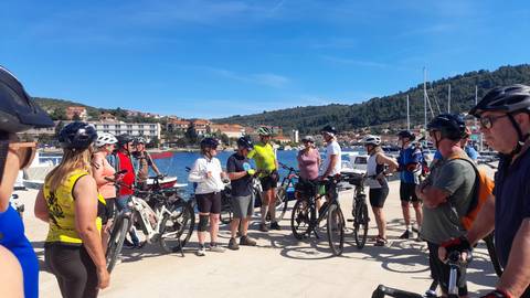 Cycling group gathers on a sunny marina pier for a briefing with boats behind.