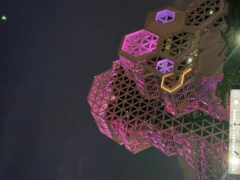 A striking modern hexagonal building lit with vivid pink and purple lights against the night sky.