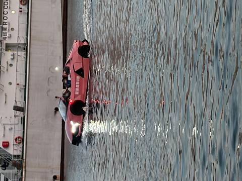 A pink amphibious car-boat with passengers cruises across reflective evening water.