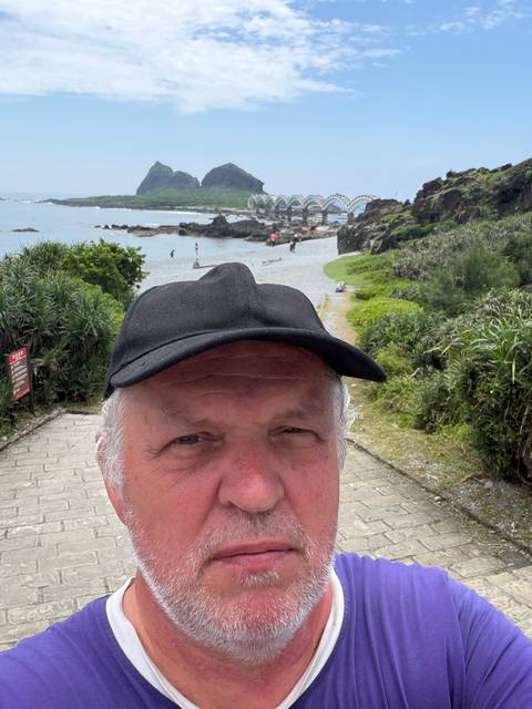 Selfie with a man’s face dominating the foreground and a rocky beach and sea behind.