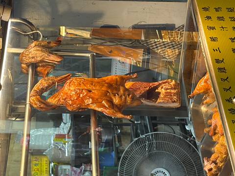 Roast ducks and meats hang in a glass-front street food stall under warm lighting.
