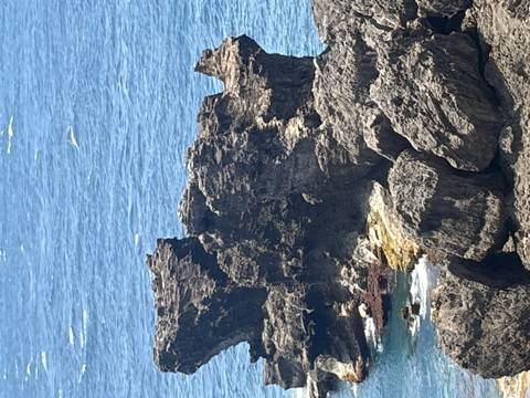 Craggy coastal rock formations meet deep blue ocean under bright sunlight.